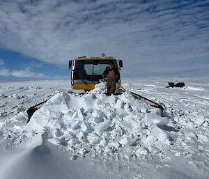 A man stands on the snow in front of a snow groomer moving snow at Woop Woop skiway