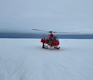 A red helicopter sitting on the ice under cloudy skies