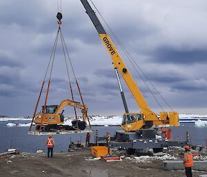 A wharf crane lifting an excavator construction vehicle to bring it onshore