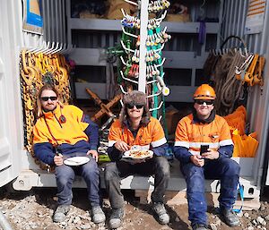 Three cargo workers on their lunch break, sitting in the opening of a shipping container used for storage