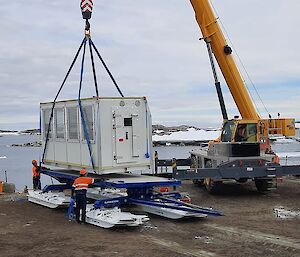 A wharf crane lifting a demountable accommodation unit onto a sled-mounted platform for transport