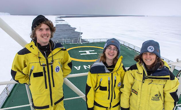 three people stand on deck of ship moving through ice