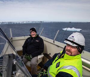 two men on deck of the ship with glacier in background