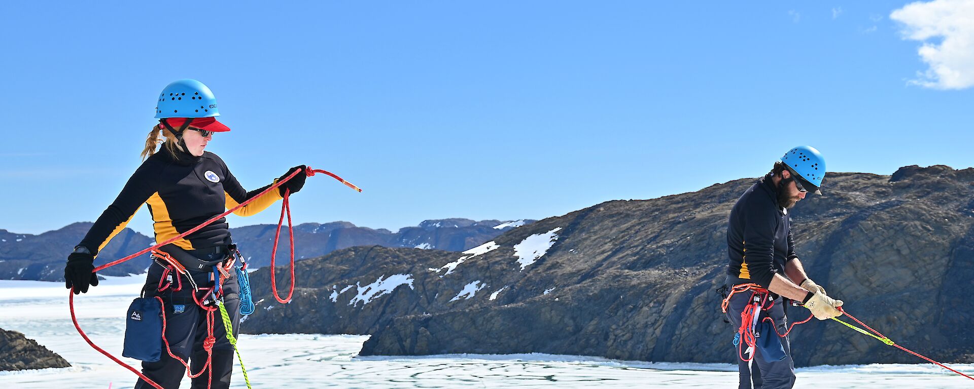 One man and one woman in climbing harnesses with ropes on the top of an ice cliff