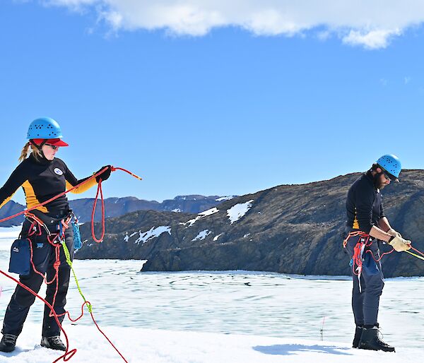 One man and one woman in climbing harnesses with ropes on the top of an ice cliff