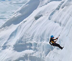 A woman rappelling down an ice cliff with a rope and harness