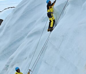 Two men climbing an ice cliff with harnesses, ropes and ice axes