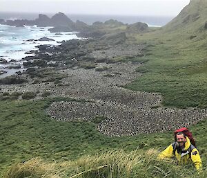 A man stands at the top of a steep and grassy hill.