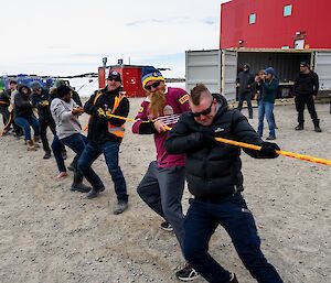 About 10 station members pulling hard on one end of a bright orange rope in a game of Tug-of-War