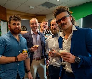 A photo of 5 smartly-dressed station members, holding beverage glasses or cans, smiling for the camera