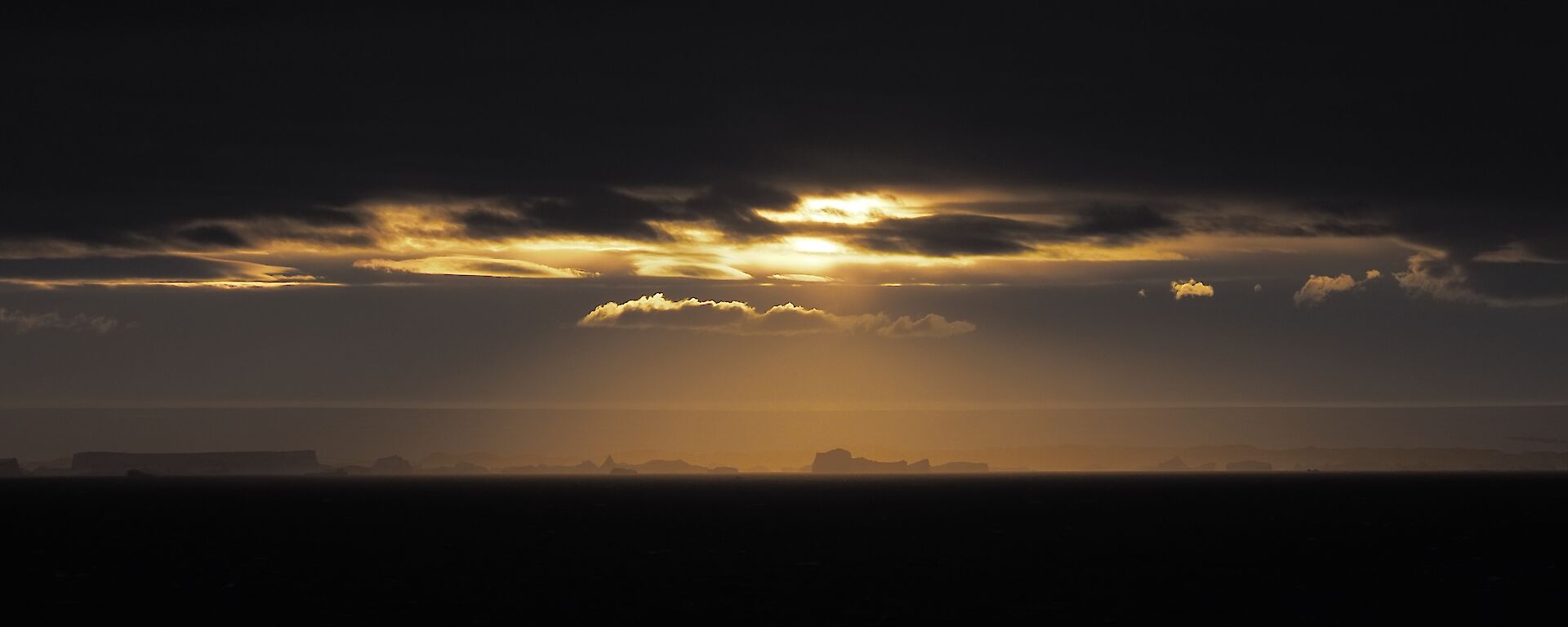 A stunning view from the plateau of icebergs in a golden light as the sun peaks through a moody dark sky