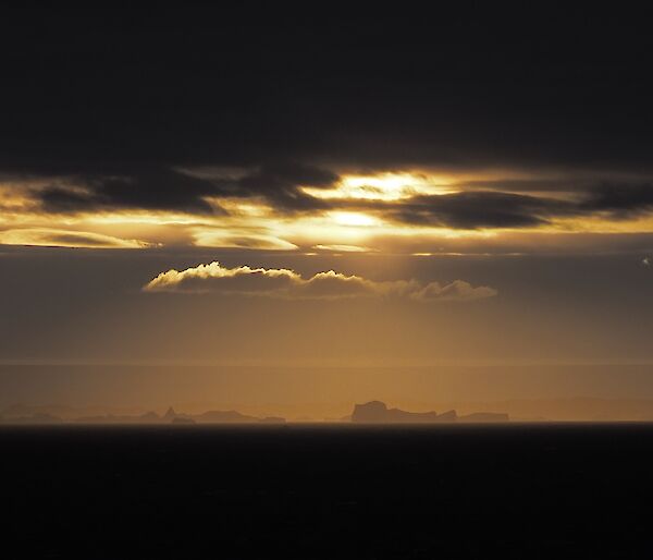 A stunning view from the plateau of icebergs in a golden light as the sun peaks through a moody dark sky