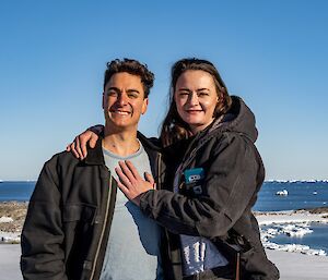 A couple smile with a blue sky behind them