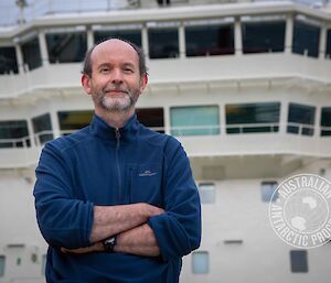 A man smiling with a ship behind him