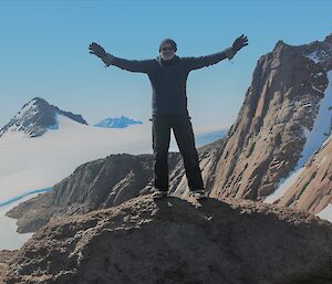 An expeditioner, Billy Merrick, with arms outstretched on a rock above Patterned Lake in the Central Masson range near Mawson