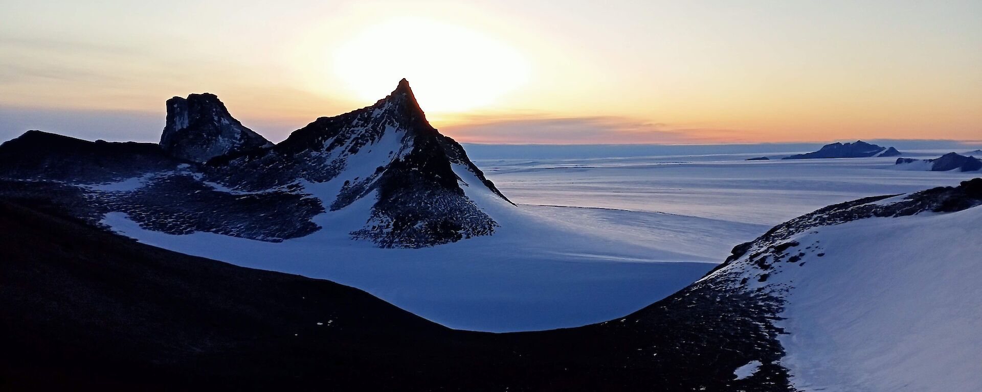 A stunning view of Fang Peak from Mt Elliot, with a winter sun in the background