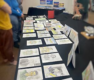 A long table laid out with several watercolour sketches. People are standing around the table, looking down at the sketches