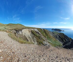 A green hill runs down to the foreshore under a bright sun