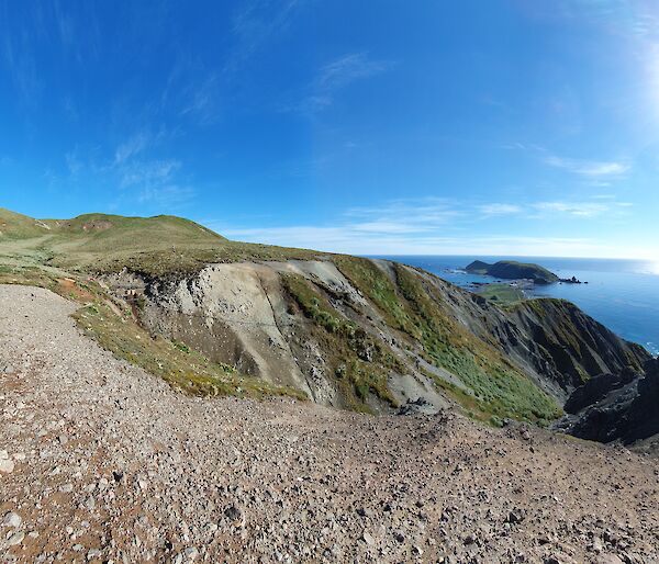 A green hill runs down to the foreshore under a bright sun