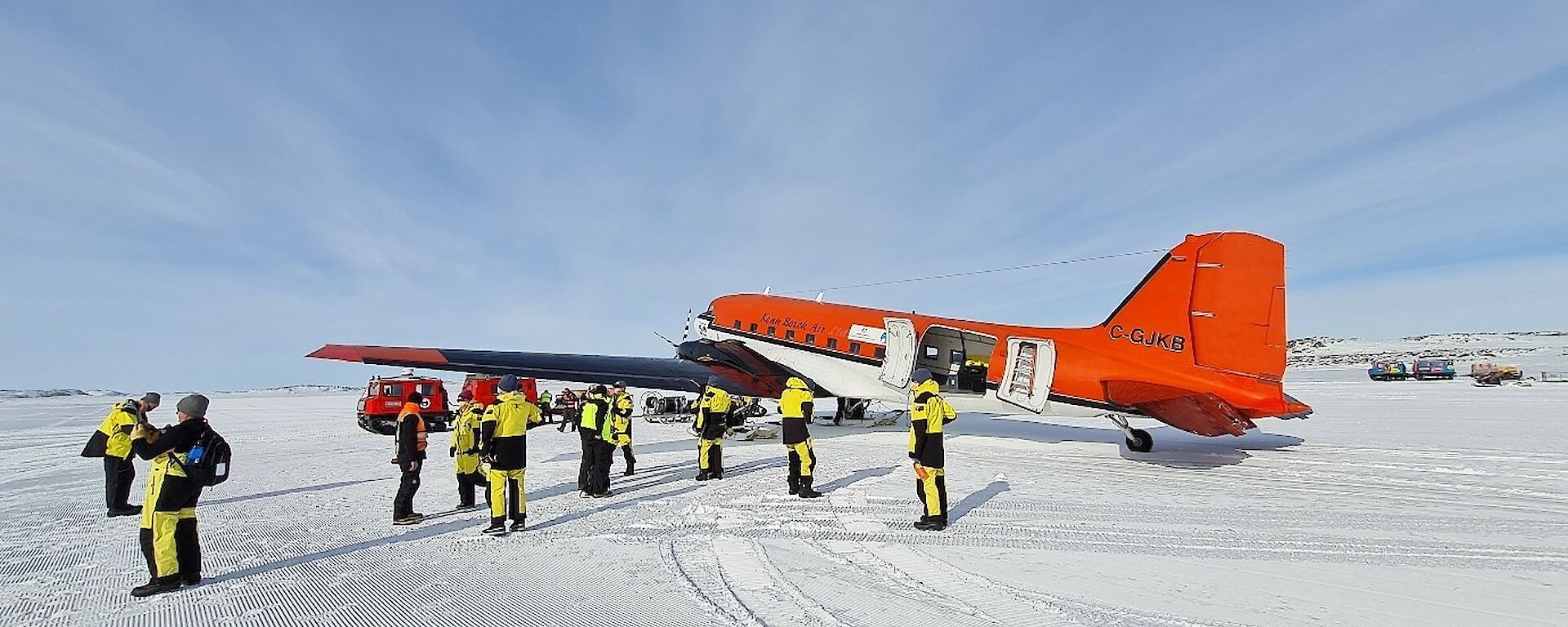 A group of expeditioners on the ice with a red plane in the background