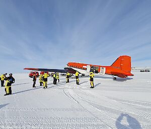 A group of expeditioners on the ice with a red plane in the background