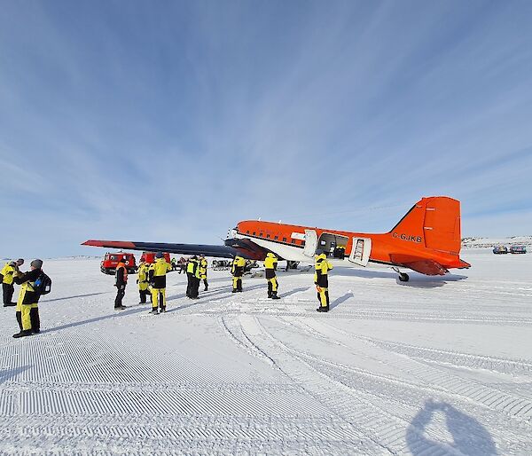 A group of expeditioners on the ice with a red plane in the background