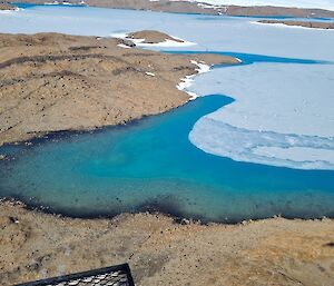 An aerial photo of a blue lake half frozen and some rocky ground