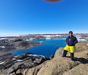 A man standing on rocks with a large lake and some snow in the background