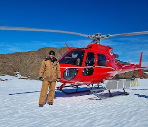 A man standing in work clothes in front of a red helicopter on the ice