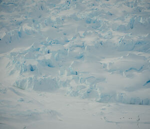 A zoomed-in view of sea/glacier ice, in smooth curves alternating with steep, tooth-like ridges. Some seals are gathered in the lower right corner - visible only as tiny specks on a smooth part of the ice.