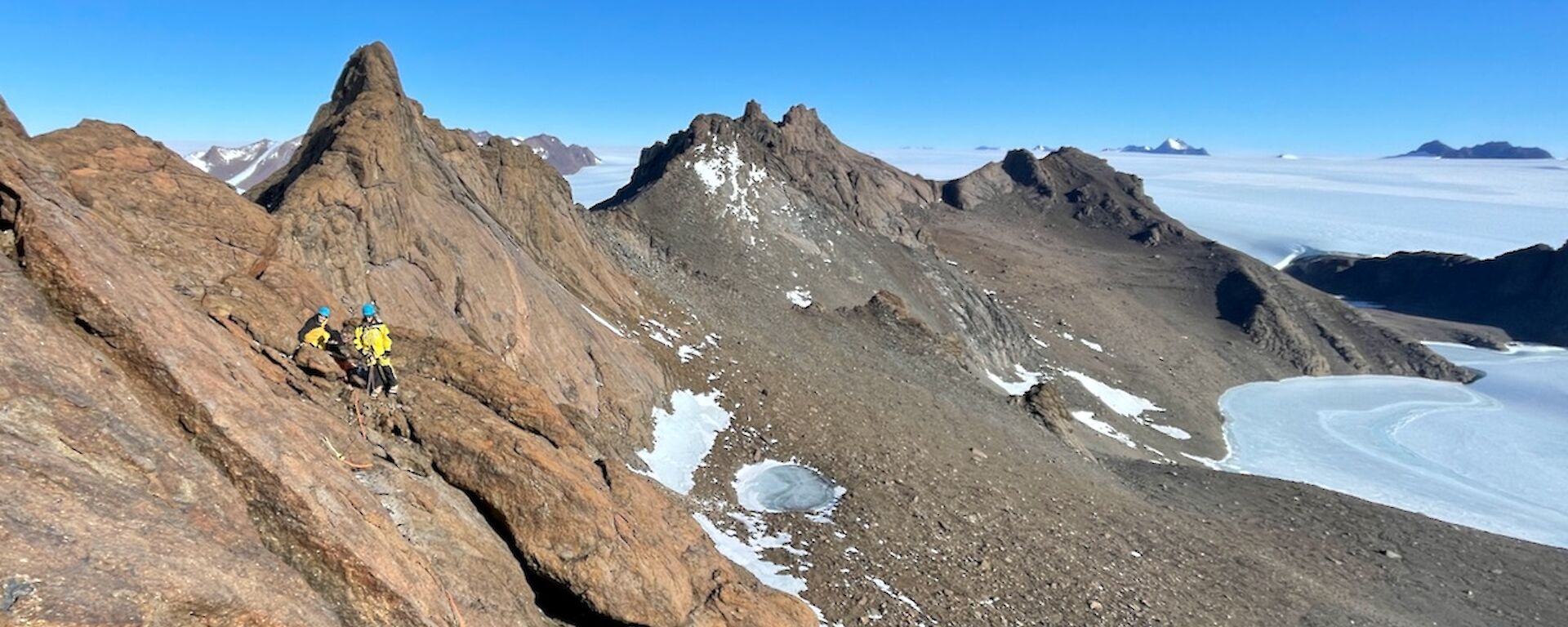 A spectacular view from Rumdoodle summit looking west, with expeditioners in the foreground nearly at the peak on a beautiful Mawson Day