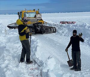 2 people in the snow with machinery in the background