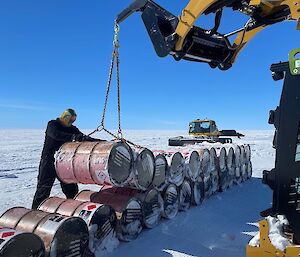 A man with around 20 pink fuel drums stacked on the snow