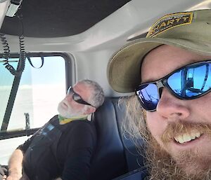 One person asleep with another person taking a selfie in a vehicle