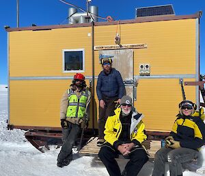 4 people sitting outside a container shelter on the snow