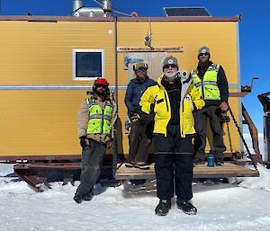 4 people standing outside a container shelter on the snow