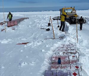 3 people digging fuel drums out of the snow