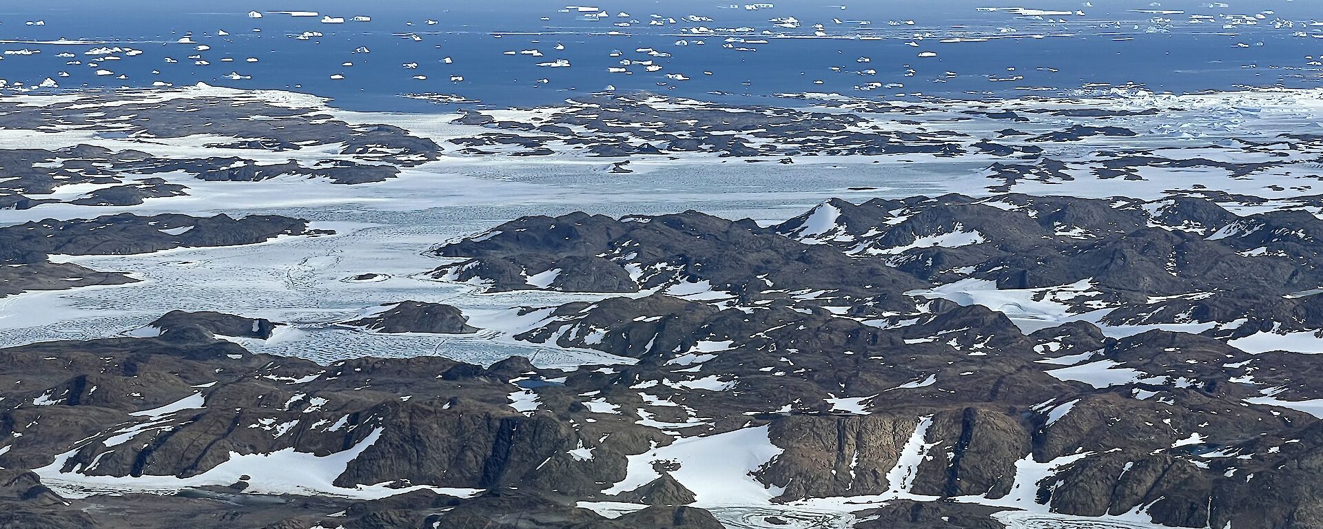 Aerial view of the Vestfold Hills showing rocky ground and a small covering of snow with the ocean present behind