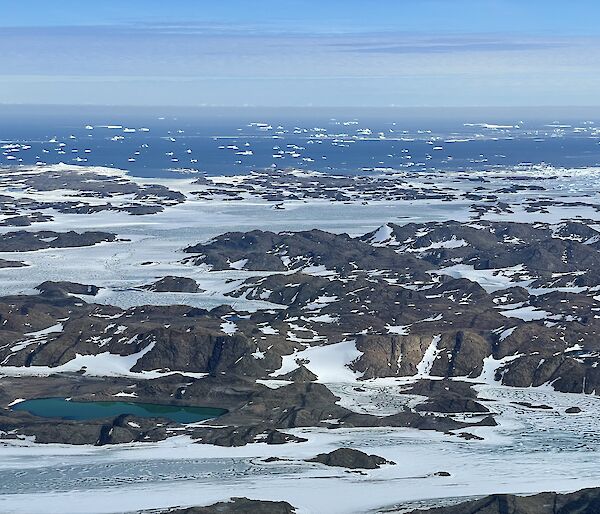 Aerial view of the Vestfold Hills showing rocky ground and a small covering of snow with the ocean present behind