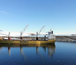 A bright yellow cargo ship in the sea with ice behind it
