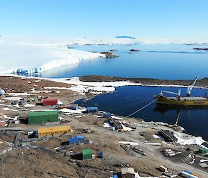 A ship sits next to the research station in the ocean with the icy plateau in the distance