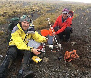 Two men working on a seismometer in the black soil
