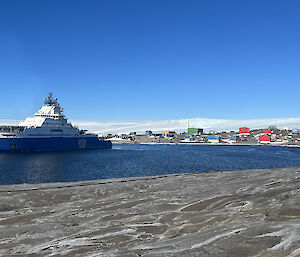 A blue and white ship sits int he harbour in front of the station's colourful buildings