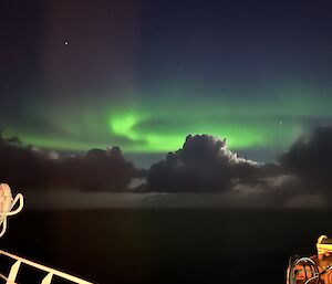 A green aurora is visible from the stern of the ship
