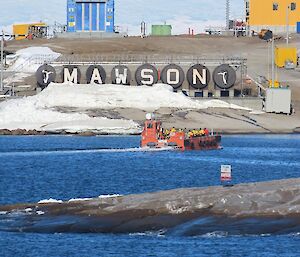 A red barge takes supplies past a large sign naming Mawson station