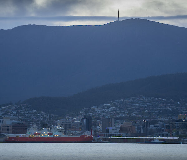 ship in harbour at dusk with mountain and city in background