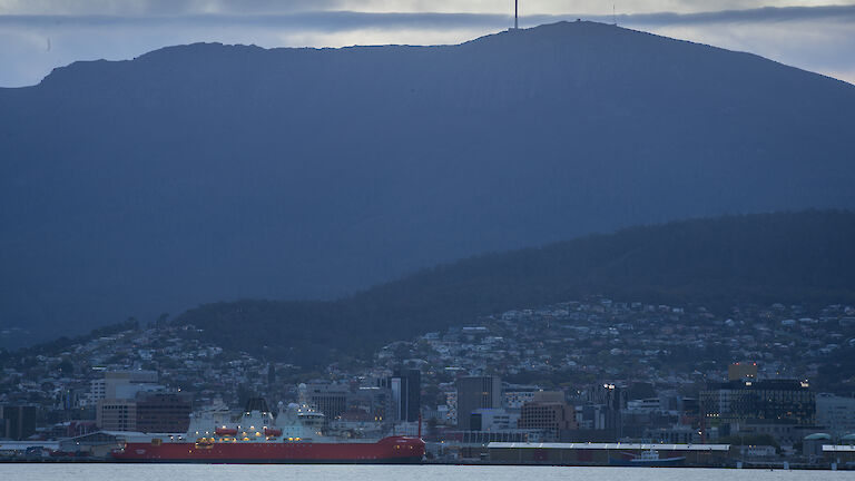 ship in harbour at dusk with mountain and city in background