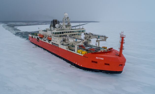 orange ship moving through ice covered sea