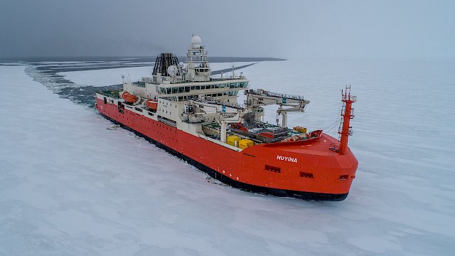 orange ship moving through ice covered sea