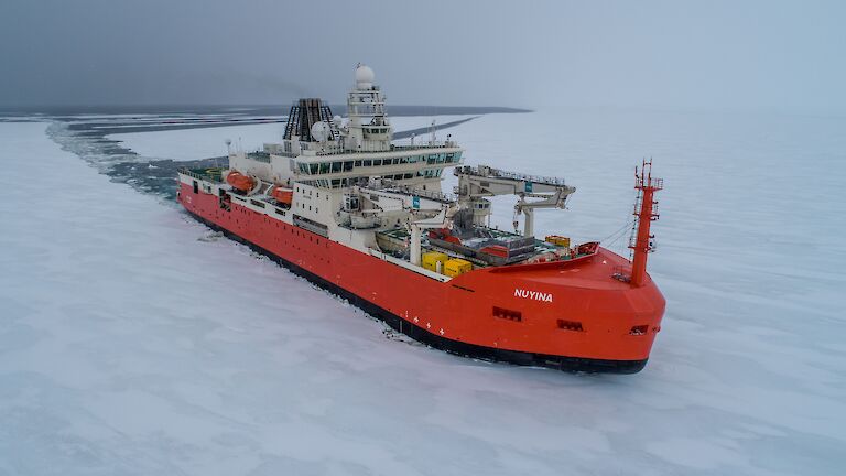 orange ship moving through ice covered sea